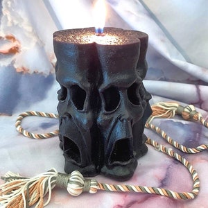 May include: A black candle with a skull design is lit and surrounded by a decorative rope with tassels.