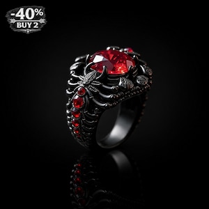 Puede incluir: Un anillo negro con una gran gema roja facetada en el centro. El anillo tiene un intrincado trabajo de metal oscuro con piedras rojas más pequeñas y detalles decorativos. El texto "-40%" y "BUY 2" es visible.