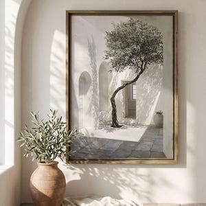 May include: A framed painting depicts a sunlit courtyard with a tree. The artwork features a gold frame, white walls, and a stone floor. A terracotta vase with greenery sits in the foreground. The scene evokes a Mediterranean aesthetic.