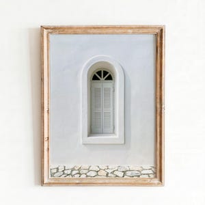 Puede incluir: Impresión enmarcada que muestra una pared blanca con una ventana arqueada y contraventanas. La ventana está pintada de gris claro y el marco es de color marrón claro. Un borde de piedra se encuentra en la parte inferior de la pared.