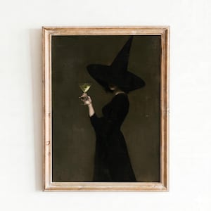Puede incluir: Una impresión de arte mural enmarcada que representa una figura con vestido negro y sombrero de ala ancha y punta, sosteniendo una copa de martini con un líquido verde pálido sobre un fondo de color verde oliva oscuro y apagado.