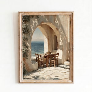 Puede incluir: Una lámina de arte enmarcada que muestra un arco de piedra con vistas a un mar azul en calma. Bajo el arco, una mesa de madera y dos sillas se asientan sobre un patio de piedra. Follaje verde trepa por la estructura de piedra clara.
