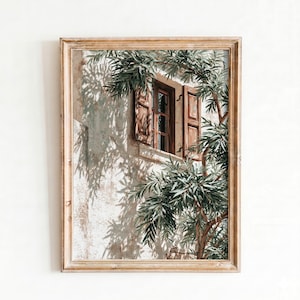May include: A framed print of a sunlit window with open wooden shutters. Green foliage frames the window, casting shadows on the textured, off-white wall. The artwork evokes a Mediterranean or Tuscan aesthetic.
