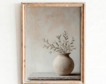 May include: A framed wall art print featuring a round, beige ceramic vase holding a sprig of green olive branches. The vase sits on a flat, stone-like surface against a soft, neutral-toned background with a light, mottled texture.