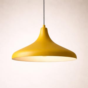 May include: A modern, yellow pendant light fixture with a flared shade. The light hangs from a black cord and illuminates with a warm, soft glow. The fixture has a smooth, matte finish and a simple, elegant design.