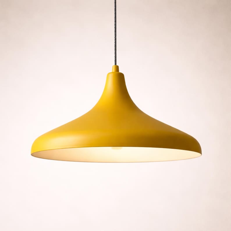 May include: A modern, yellow pendant light fixture with a flared shade. The light hangs from a black cord and illuminates with a warm, soft glow. The fixture has a smooth, matte finish and a simple, elegant design.