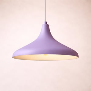 May include: A lavender-colored pendant light fixture with a flared shade. The light hangs from a white cord and illuminates a soft, warm glow. The fixture has a smooth, matte finish and a simple, modern design.