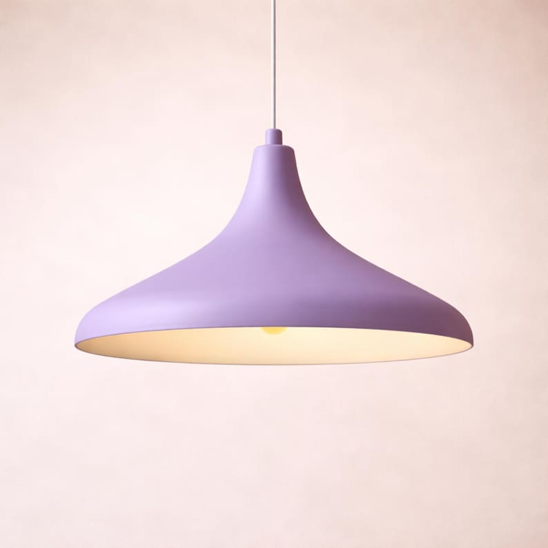May include: A lavender-colored pendant light fixture with a flared shade. The light hangs from a white cord and illuminates a soft, warm glow. The fixture has a smooth, matte finish and a simple, modern design.