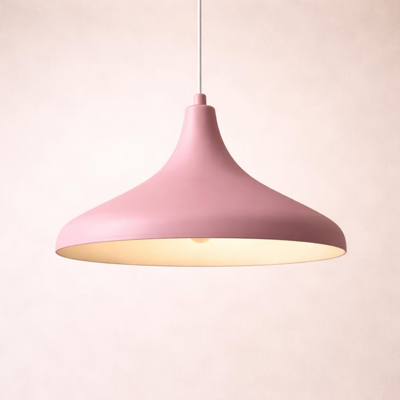 May include: A pink pendant light fixture with a wide, flared shade. The light hangs from a white cord and has a soft, warm glow emanating from the underside. The fixture has a smooth, matte finish.