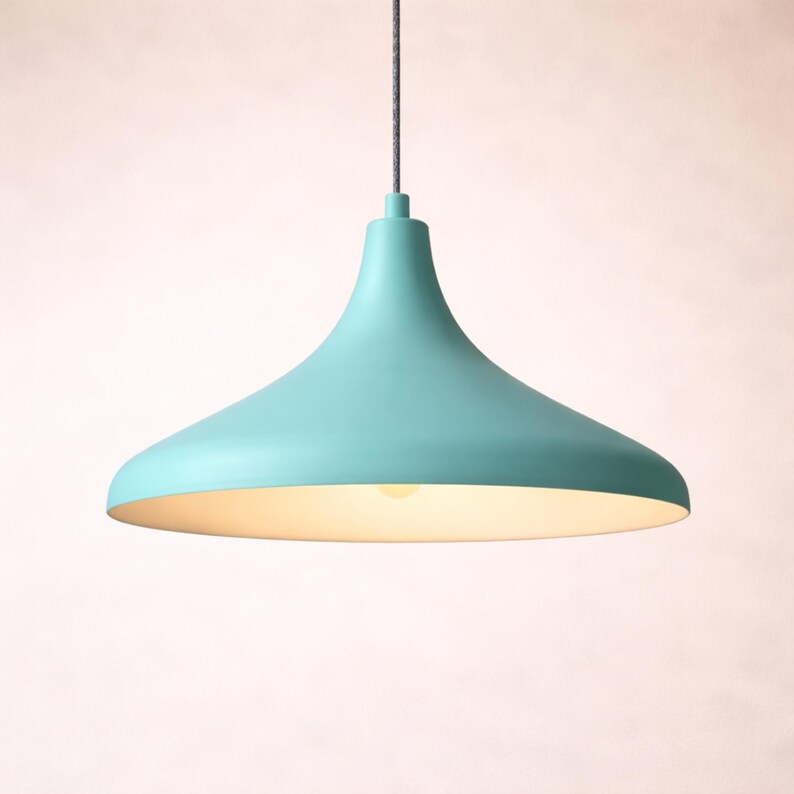 May include: A teal-colored pendant light fixture with a flared shade. The light hangs from a gray cord and has a soft, warm glow emanating from the bottom. The fixture has a smooth, matte finish and a simple, modern design.