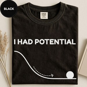 Könnte beinhalten: Ein schwarzes T-Shirt mit Rundhalsausschnitt und dem weißen Schriftzug I HAD POTENTIAL auf der Brust. Unter dem Text befindet sich eine weiße grafische Darstellung einer geschwungenen Flugbahn, die in einem Kreis als Ball endet.