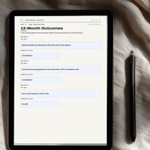 May include: A digital tablet displaying a 12-Month Outcomes planning page with text fields for goals and values, including entries for ranking, program delivery, and running, accompanied by a black stylus pen resting on the right side of the screen.