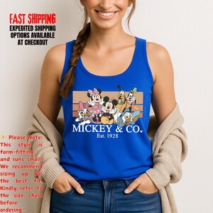 Puede incluir: Una camiseta sin mangas azul real con un gr&aacute;fico de Mickey Mouse y sus amigos. El gr&aacute;fico incluye a Mickey, Minnie, Donald, Daisy, Goofy y Pluto, con el texto "MICKEY & CO. Est. 1928". La camiseta tiene cuello redondo y la lleva una persona.
