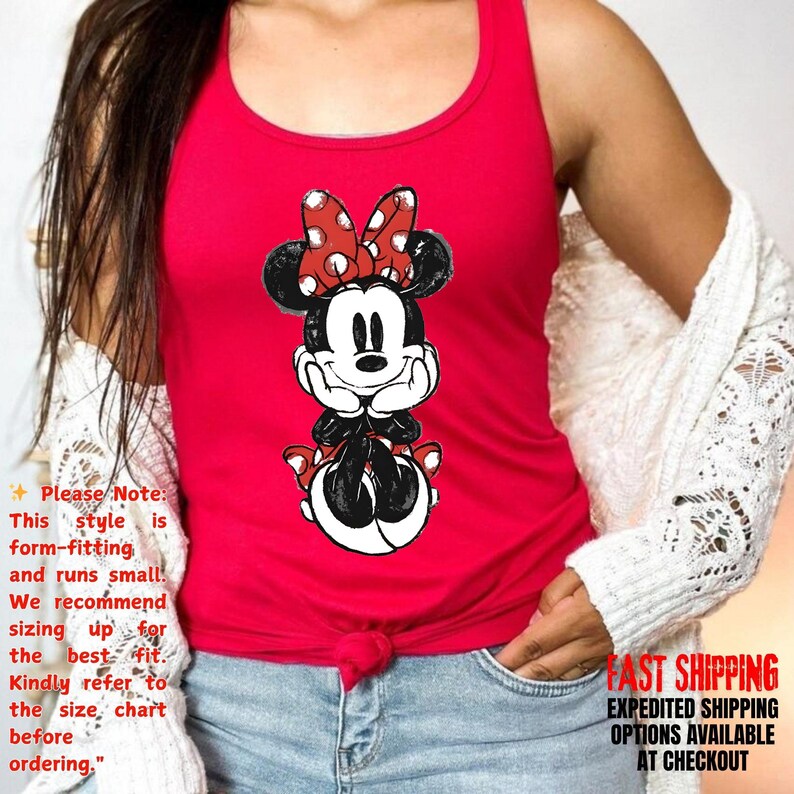 May include: Red tank top featuring a Minnie Mouse graphic. The graphic shows Minnie Mouse with a red bow with white polka dots. The tank top has a scoop neck and is form-fitting. The text on the image says, "Please Note: This style is form-fitting and runs small."