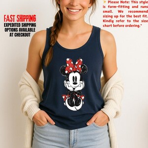 May include: Navy blue tank top featuring a Minnie Mouse graphic with a red bow and polka dots. The text "FAST SHIPPING EXPEDITED SHIPPING OPTIONS AVAILABLE AT CHECKOUT" is printed on the left side. The text "Please Note: This style is form-fitting and runs small..." is on the right.