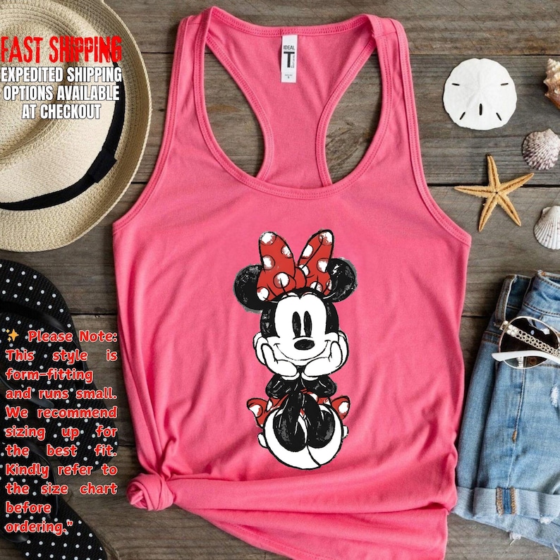 May include: A pink tank top featuring a Minnie Mouse graphic. The cartoon character is depicted with a red bow with white polka dots. The tank top has a racerback design and is made of a soft material.