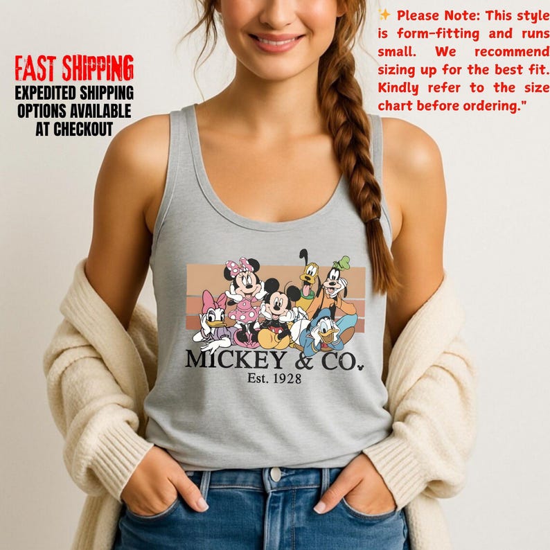 Puede incluir: Una camiseta sin mangas gris con un gr&aacute;fico de Mickey Mouse y sus amigos, con el texto "MICKEY & CO. Est. 1928". La camiseta sin mangas tiene cuello redondo y est&aacute; hecha de un material suave. La imagen tambi&eacute;n incluye texto sobre tallas.