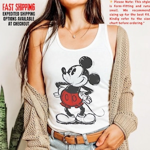 May include: White tank top featuring a black and red Mickey Mouse graphic. The cartoon character is in a classic pose with hands on hips. The tank top has a scoop neck. The text "FAST SHIPPING EXPEDITED SHIPPING OPTIONS AVAILABLE AT CHECKOUT" is in the upper left corner.