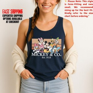 Puede incluir: Camiseta sin mangas azul marino con un gr&aacute;fico de Mickey Mouse y sus amigos, con el texto "Mickey & Co. Est. 1928". La camiseta sin mangas tiene el texto "FAST SHIPPING EXPEDITED SHIPPING OPTIONS AVAILABLE AT CHECKOUT" en el lado izquierdo.