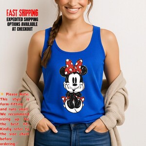 May include: A royal blue tank top featuring a Minnie Mouse graphic. The graphic shows Minnie Mouse with a red polka dot bow, black ears, and a black and white outfit. The tank top is sleeveless and made of a soft material.