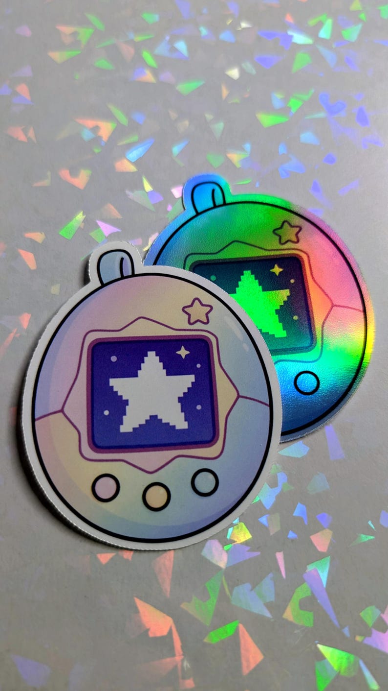 May include: Two holographic stickers in the shape of a retro handheld game. One sticker is a pastel purple and blue, the other is green and blue. Each has a star graphic on the screen and a star-shaped outline.