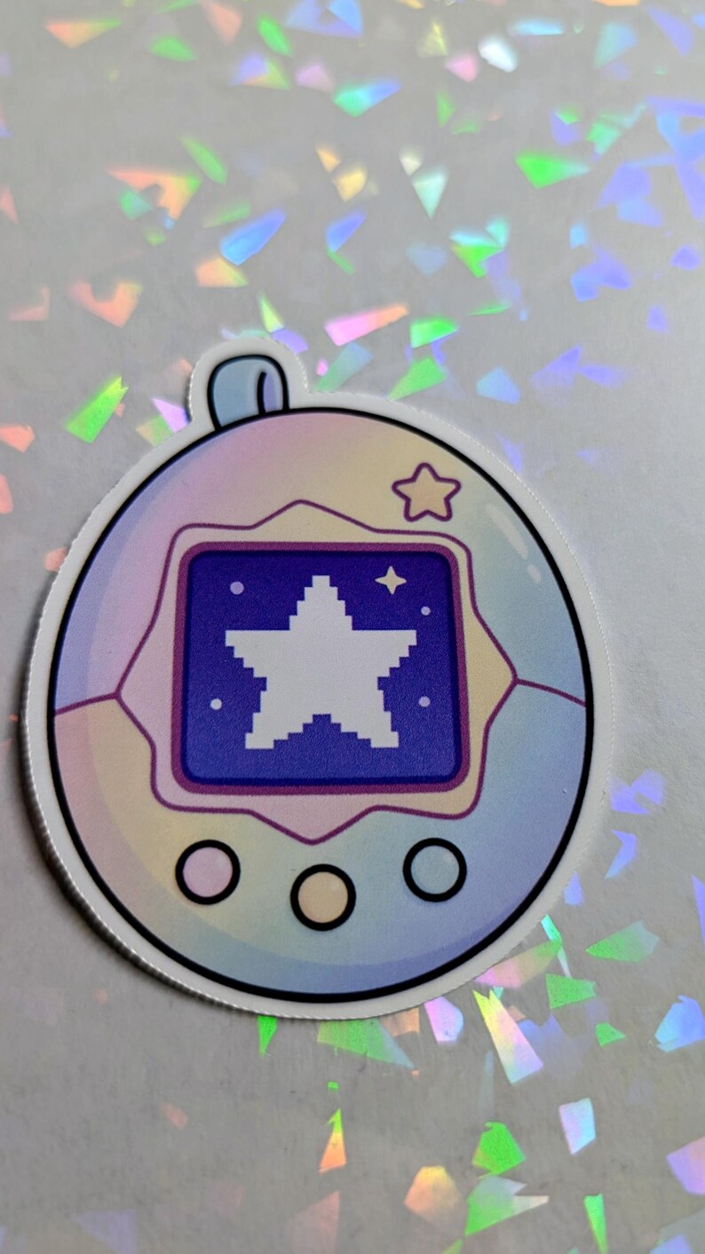 May include: A sticker featuring a retro-style digital pet device. The device has a blue screen displaying a white pixelated star. The casing is a gradient of pastel colors, with a small star icon at the top. Three black circles are at the bottom.