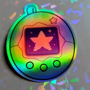 May include: Holographic sticker featuring a pixelated star design within a square, surrounded by a circular frame. The sticker has a rainbow color scheme with a star and three circles at the bottom. A small star is at the top.