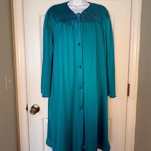May include: Teal-colored vintage robe with long sleeves and a button-down front. The robe features dark blue trim on the collar, cuffs, and hem. Decorative embroidery accents the neckline. The robe is displayed on a white mannequin.