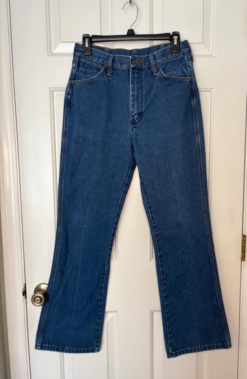 Op de afbeelding: Blauwe denim jeans met een klassiek ontwerp met vijf zakken en een lichte flare aan de zoom. De jeans hangen aan een zwarte hanger tegen een witte deur. De jeans zijn gemaakt van stevig denim materiaal.
