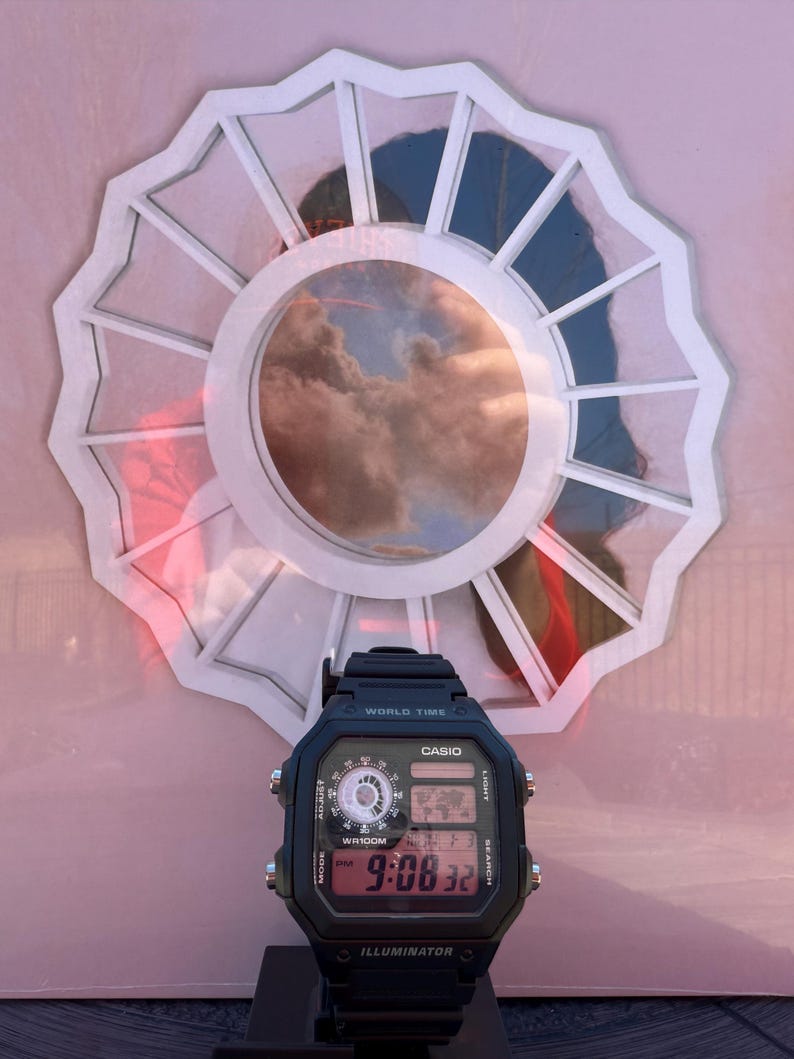 May include: Black Casio digital watch with a rectangular face, displaying the time 9:08:32. The watch is positioned in front of a white, scalloped-edged circular design with a cloudy sky reflected in the center.