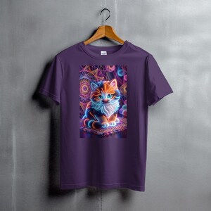 May include: Purple t-shirt featuring a vibrant graphic of a neon-style kitten. The cat has orange and blue fur with a white chest, set against a colorful geometric background. The shirt is hanging on a wooden hanger.