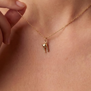 May include: A delicate gold necklace featuring a small, detailed tooth pendant. The pendant is a realistic representation of a molar, with visible roots and enamel. The necklace chain is fine and elegant, creating a minimalist and stylish look.