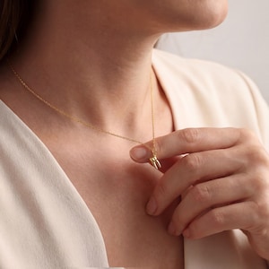K&ouml;nnte beinhalten: Goldfarbene Halskette mit einem Anh&auml;nger in Form eines Backenzahns. Der Zahnanh&auml;nger h&auml;ngt an einer zarten Goldkette. Die Halskette wird vor einem neutralen Hintergrund gezeigt.
