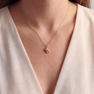 K&ouml;nnte beinhalten: Eine goldfarbene Halskette mit einem kleinen Zahnanh&auml;nger. Der Anh&auml;nger ist eine detaillierte Miniatur eines Backenzahns. Die Halskette ist filigran und scheint aus Gold zu sein. Der Hintergrund ist eine weiche, neutrale Farbe.