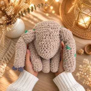 May include: A handmade, plush bunny in a soft beige colour, held in hands. The bunny has green accents and blue feet. The plush toy is made of a textured, fuzzy material. The bunny is a cute, cuddly toy.