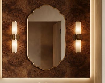 May include: A bathroom interior featuring a stone sink, brass taps, and a decorative mirror with a gold frame. The mirror is set against a wood-panelled wall, with two sconces. The space is framed by an arched ceiling and neutral-toned curtains.