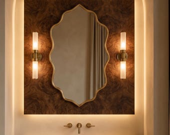 May include: A bathroom vanity featuring a gold-edged, scalloped mirror, two wall lights, and a stone countertop. The mirror is set against a dark wood-effect panel, with warm lighting illuminating the space.