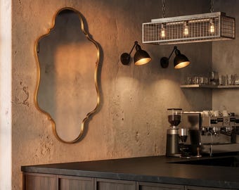 May include: An ornate gold-framed mirror hangs on a textured wall, with black sconce lights and a rectangular cage pendant light. A dark wood counter with stools and a coffee machine complete the cafe setting.