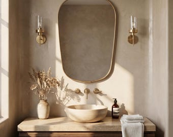 Puede incluir: Un moderno mueble de baño con un gran espejo ovalado con marco dorado. El mueble tiene un armario de madera con encimera de piedra, un lavabo y grifos dorados. Dos apliques flanquean el espejo y un jarrón con flores secas está sobre la encimera.