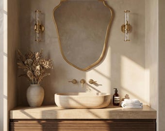May include: A bathroom interior featuring a gold-framed mirror, wall lights, and a stone basin. The vanity unit has a wooden slatted front. A vase of dried flowers and a stack of white towels complete the scene.
