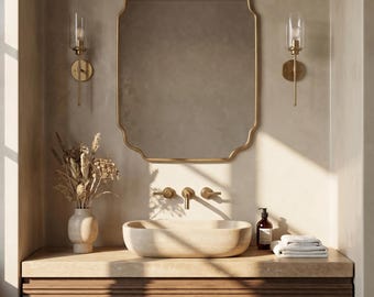 May include: A bathroom vanity featuring a gold-framed mirror, wall lights, and a stone sink. The vanity has a wooden cabinet with horizontal grooves. A vase with dried flowers and a stack of white towels are on the countertop.