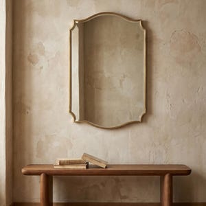 Brass mirror above wooden bench in neutral room