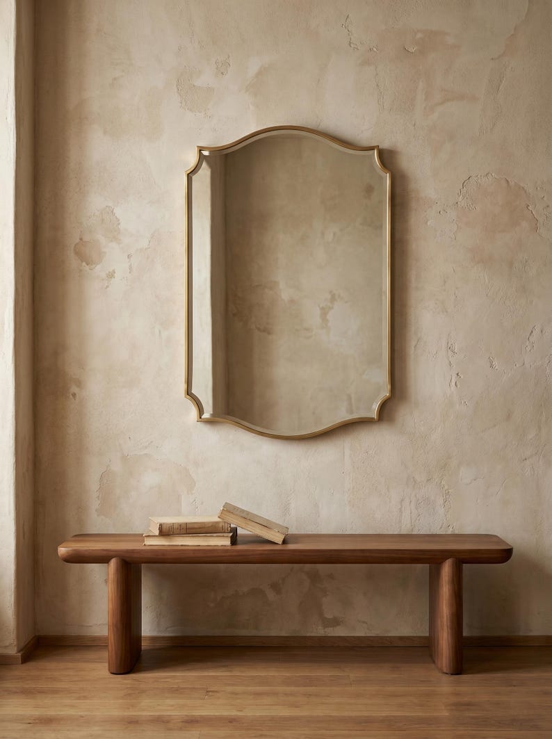 Brass mirror above wooden bench in neutral room