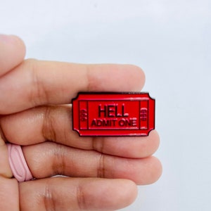 Może przedstawiać: Czerwona metalowa przypinka w kształcie biletu z czarnym tekstem, który brzmi "HELL ADMIT ONE".