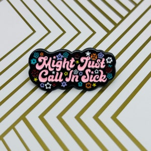 Puede incluir: Pin de esmalte negro con un texto rosa y blanco que dice "Might Just Call In Sick" rodeado de flores de colores.