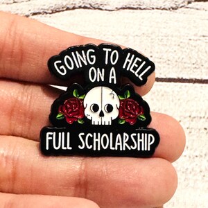 Könnte beinhalten: Schwarzer Emaille-Pin mit weißem Text "GOING TO HELL ON A FULL SCHOLARSHIP". Der Pin zeigt einen weißen Totenkopf mit roten Rosen auf schwarzem Hintergrund.