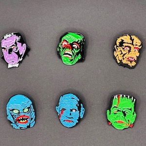 May include: Six enamel pins featuring classic monster faces. The pins include a purple vampire, a green zombie, a yellow and black creature, a blue creature, a blue zombie with a bloody eye, and a green Frankenstein's monster.