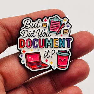 Puede incluir: Un colorido pin de esmalte con el texto "But Did You DOCUMENT it?" presenta un portátil, una portapapeles, un bolígrafo y una taza de café sonriente. El pin tiene un borde blanco y se sostiene en una mano.