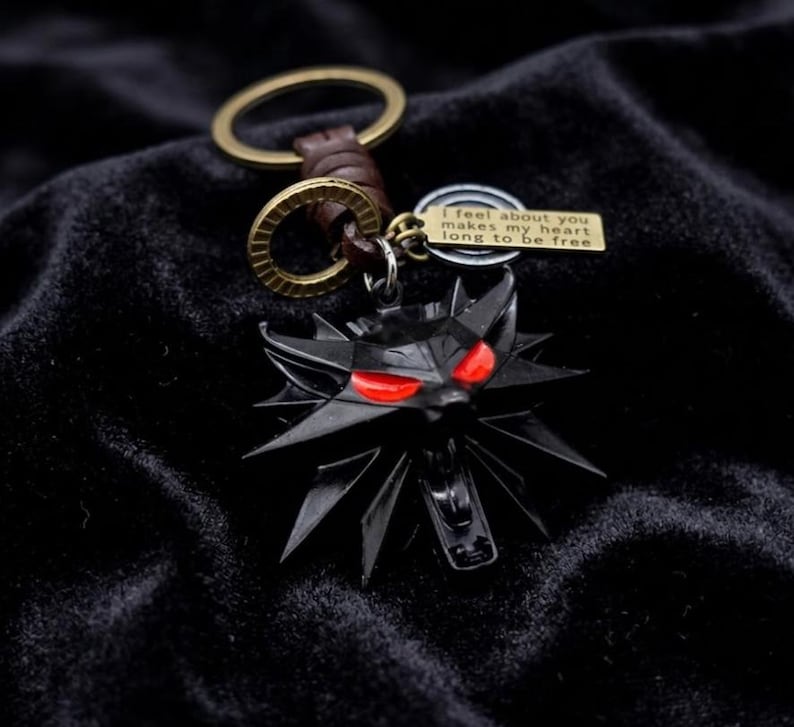 May include: Black metal keychain featuring a wolf head with red eyes. The keychain includes a small tag with the inscription "I feel about you makes my heart long to be free." The keychain has a brown leather strap and a gold-colored ring.