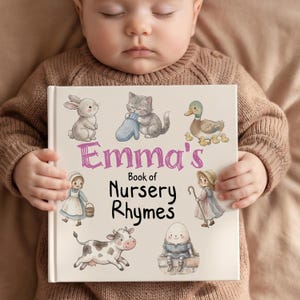 May include: A hardcover book titled "Emma's Book of Nursery Rhymes" featuring illustrations of a bunny, kitten, ducklings, a girl, a cow, and Humpty Dumpty. The cover is cream-colored with pink and black text and colorful images.